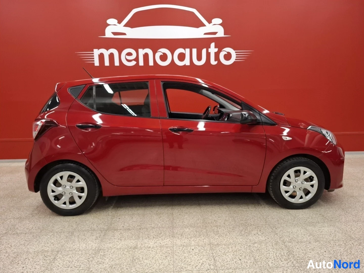 Sivulta: Hyundai i10 sivuprofiili, punainen koripinta, asemoitu myyjän tiloissa.