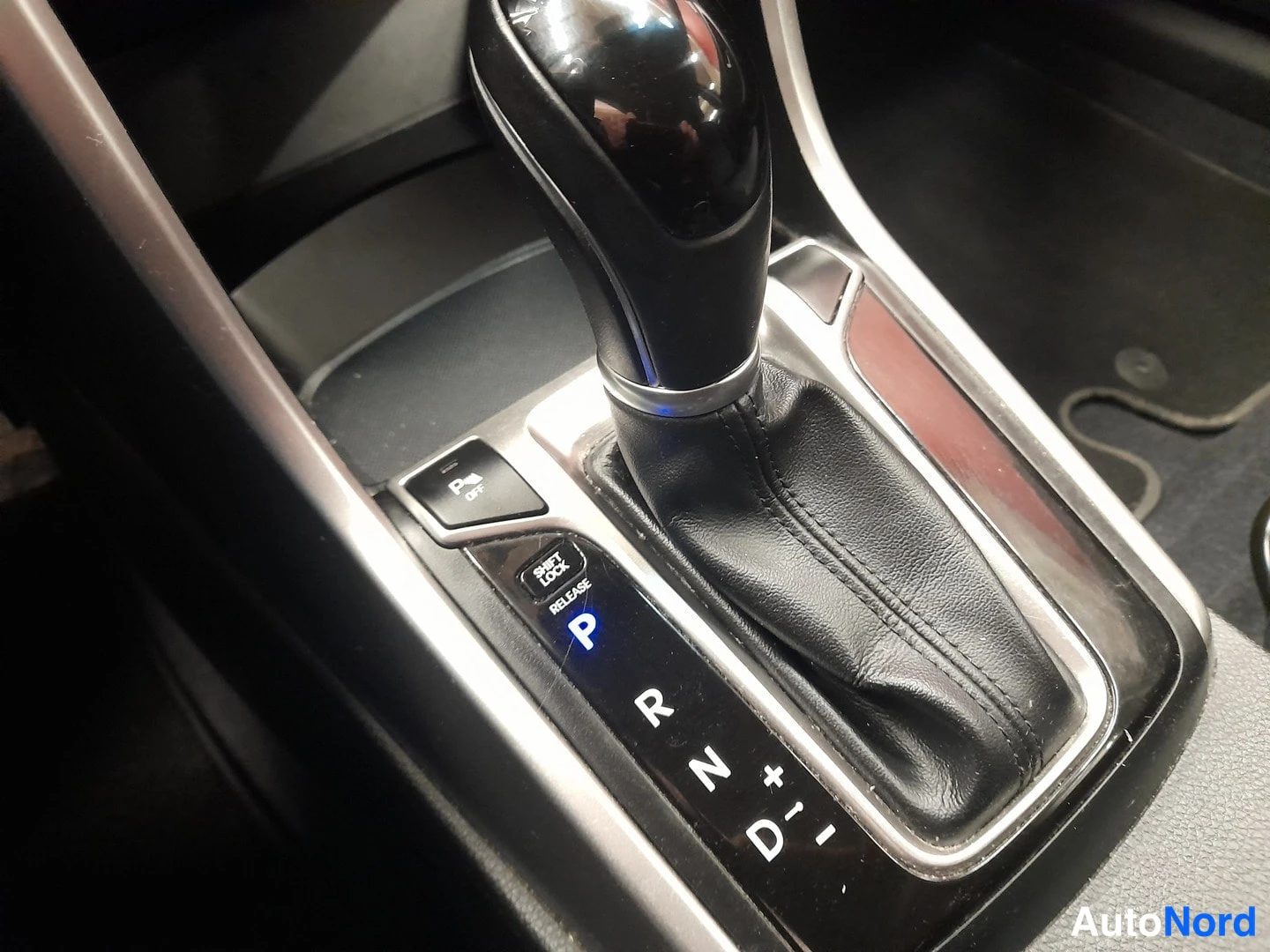 Edestä: Automaattivaihteen valitsin P-asennossa, merkinnät P R N D +/−, SHIFT LOCK RELEASE ja P/OFF-painike.