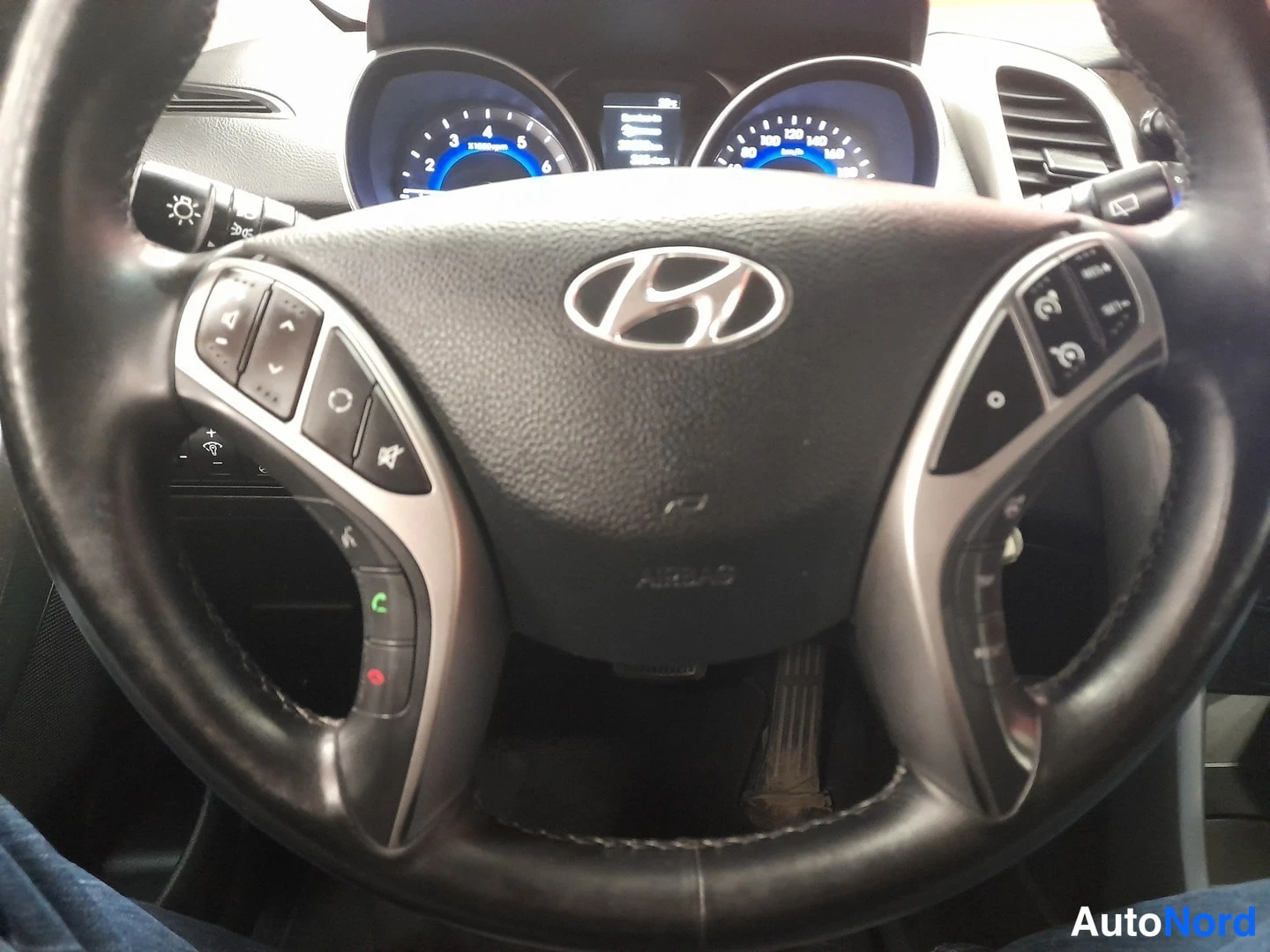 Yksityiskohta: Ohjauspyörä Hyundai-logolla, AIRBAG-teksti nuppipaneelissa, molemmin puolin monitoiminappeja, taustalla mittaristo ja ilmastointiaukoista näkyy osa tuulilasista
