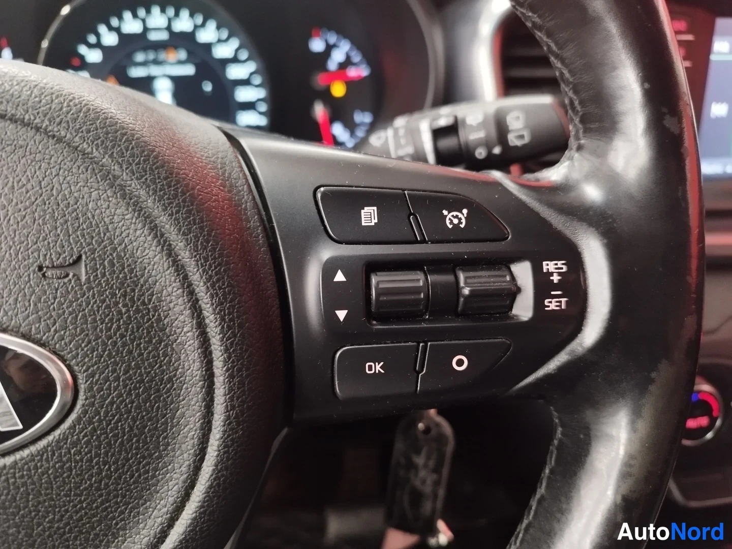 Yksityiskohta: Ohjauspyörän oikean puolen cruise control -näppäimet RES+, SET ja nopeudensäädön merkkivalot, vasemmalla Kia-tunnus.