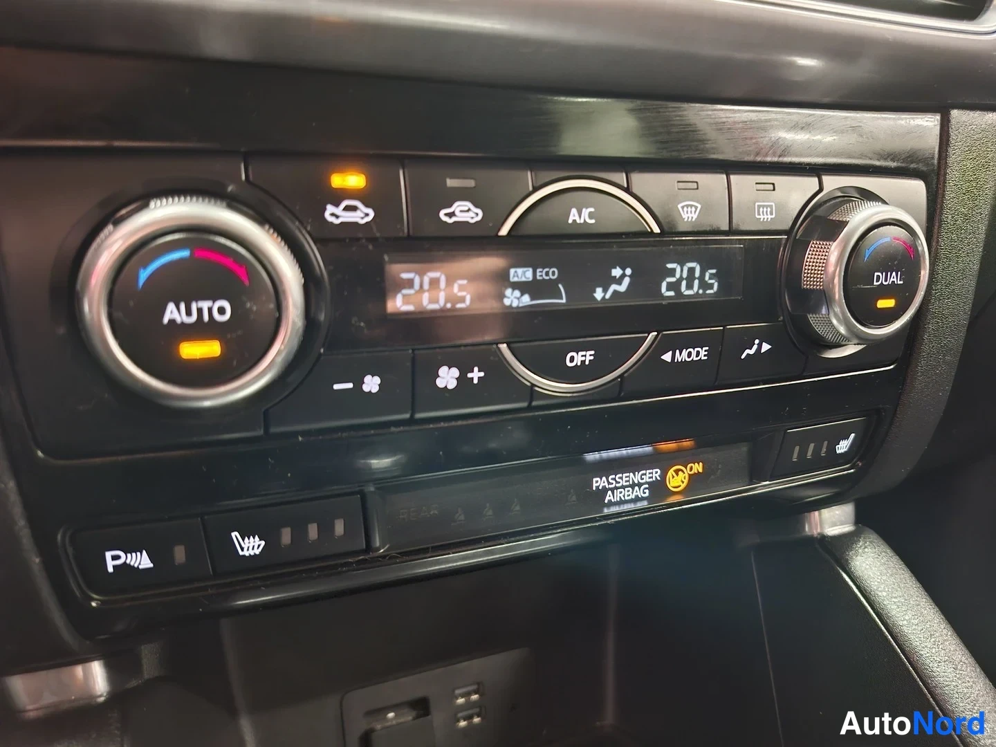 Muu: Auton ilmastoinnin säätimet kahdella napilla, näytössä lämpötilat 20,5 ja A/C, DUAL- ja AUTO-merkinnät.