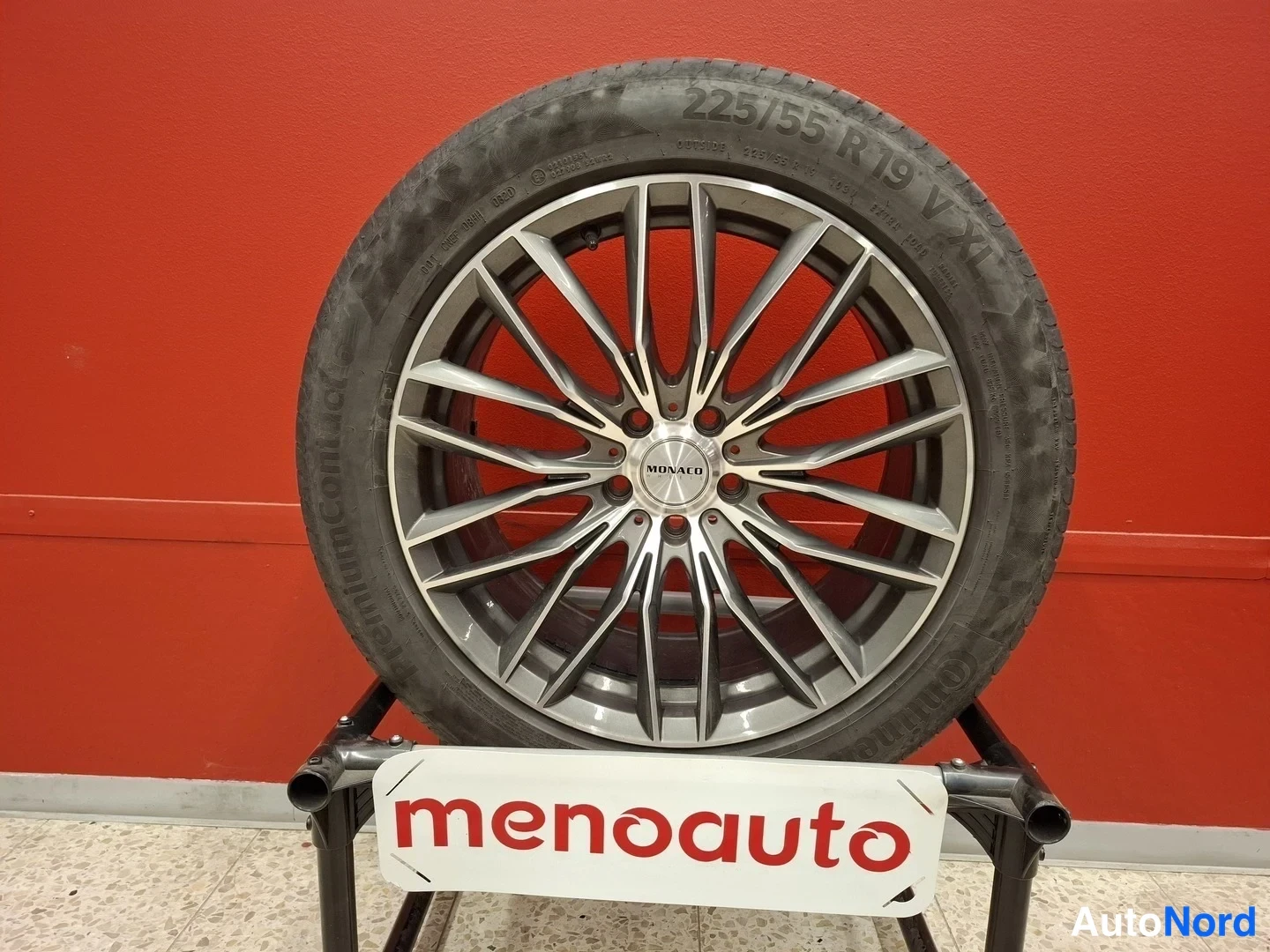 Yksityiskohta: Vanne Monaco 19 tuuman kevytmetallivanne Continuumin 225/55 R 19 V XL -renkaalla punaisella taustalla menoauto-nimikyltillä.
