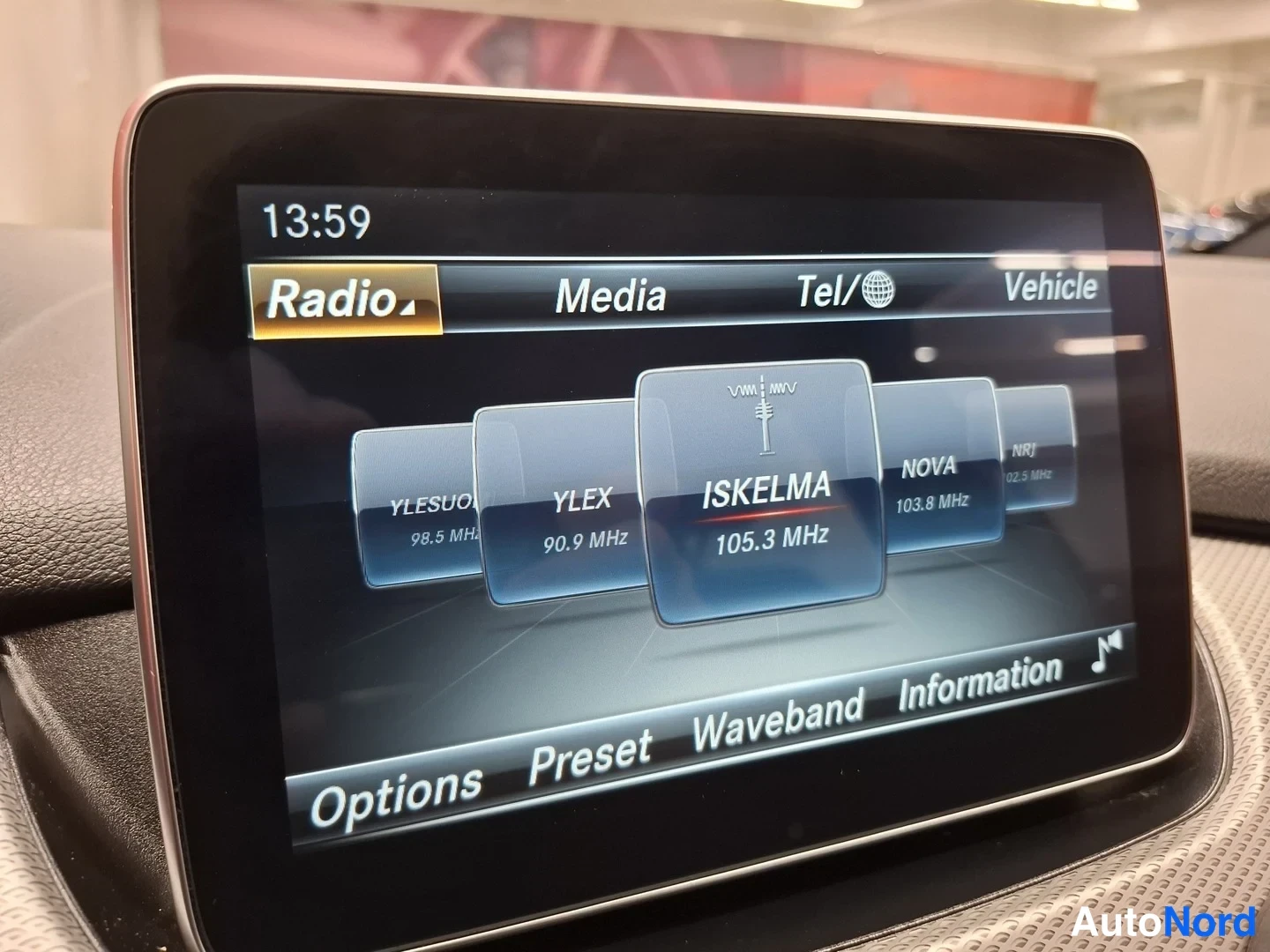 Yksityiskohta: Istumapositiivissä olevan auton näyttö radiovalikossa; kanavina muun muassa YLE Suomi, Ylex, Iskelma ja Nova, kello 13:59.