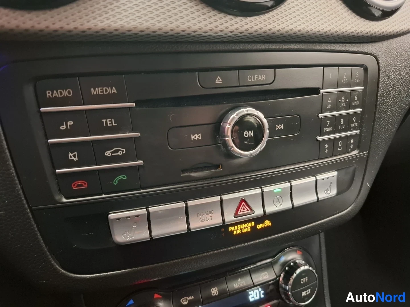 Yksityiskohta: Mercedes-Benzin kojelaudan keskikäyttöpaneeli RADIO-, MEDIA- ja TEL-napeilla, numeerisella näppäimistöllä, DYNAMIC SELECT- ja hätävilkkunapeilla sekä passengert