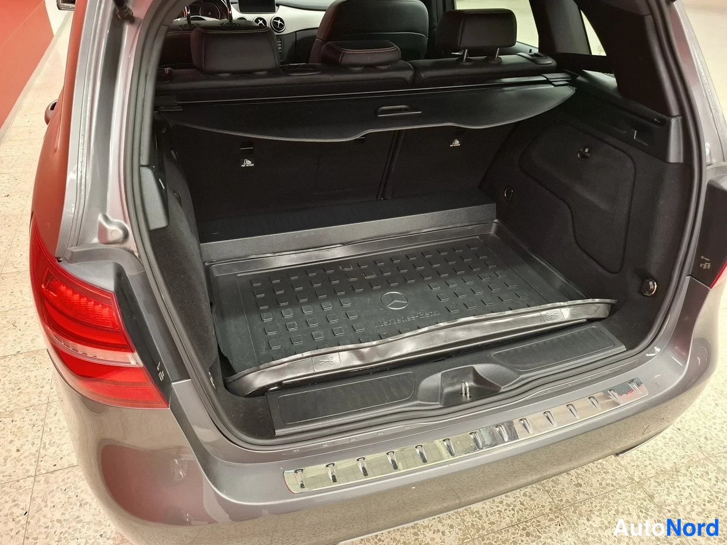 Takaa: Mercedes-Benz B:n tavaratilan kuva takaluukku auki; tumma matkalaukkuhylly, Mercedes-merkkinen muovimatto ja kromilista puskurissa.
