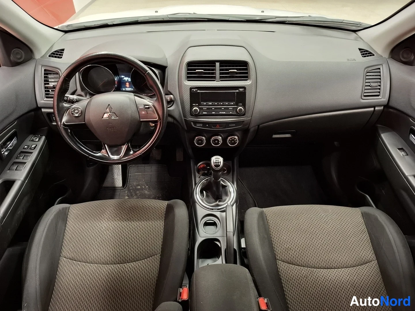 Edestä: Ohjaamo edestä: Mitsubishi-ohjauspyörä, vaihteistotanko, radio ja kaksi etuistuinta.