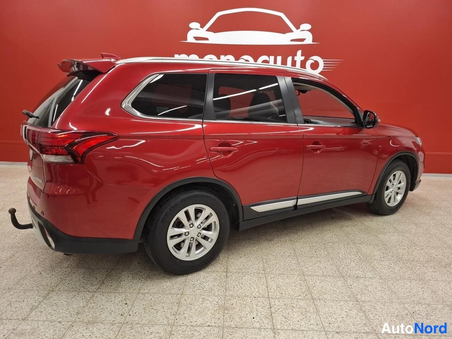 Takaviisto: Punaisen Mitsubishi Outlanderin takakulma sisätiloissa, takavaloja ja takaluukku näkyvät vasemmalla, sivu oikealla.