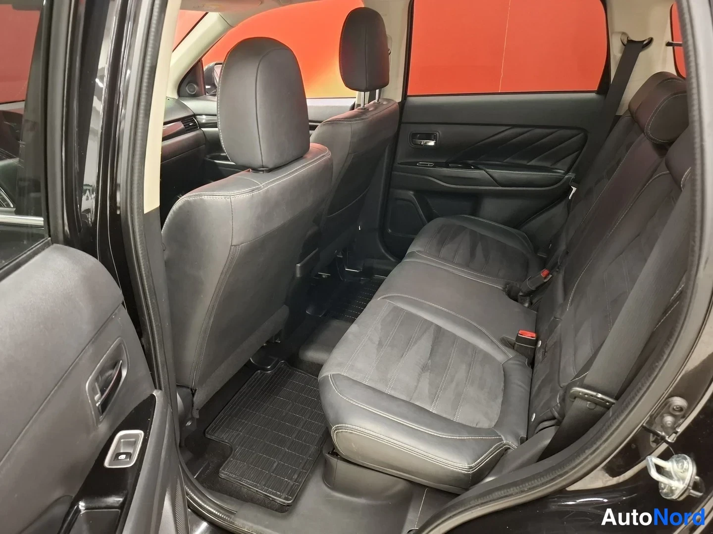 Sivulta: auton takaistuin ja sisätila kuvattu avatun oven läpi; tumma sisusta, penkillä kaksi headrest-kosketinta, oven sisäpaneelit ja lattiamatto näkyvät.