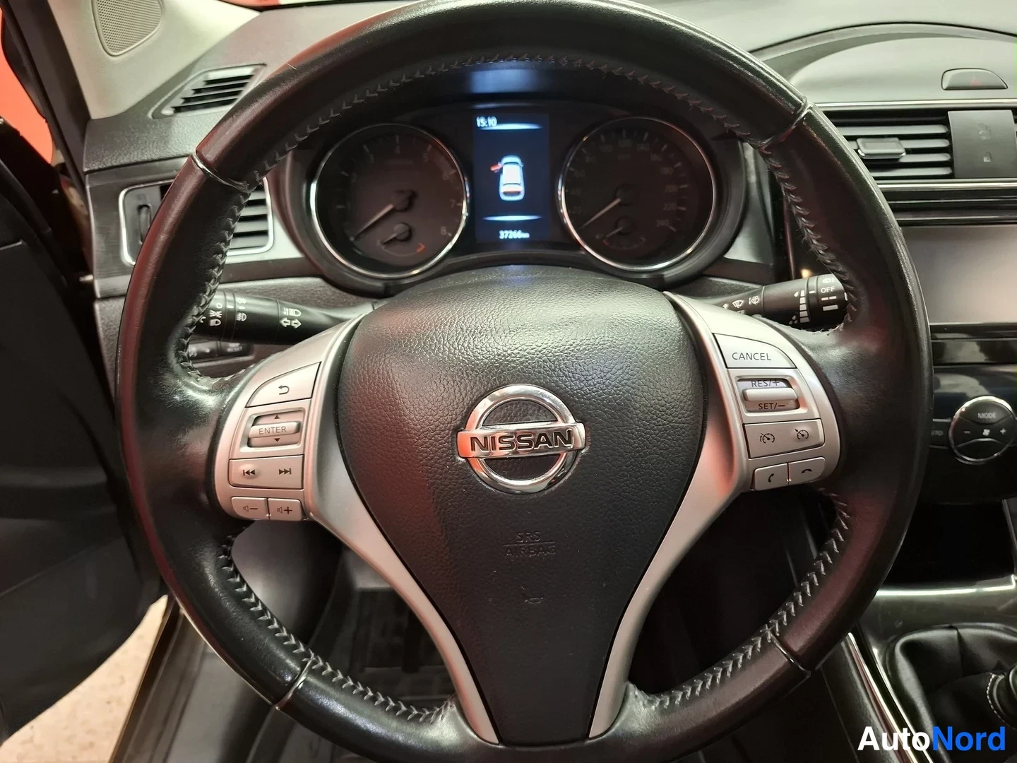 Sivulta: Nissan-ohjauspyörän lähikuva: monitoiminapit (CANCEL, RES+, SET-), taustalla mittaristossa ajetut kilometrit ja vaihdelaatikon keppi.