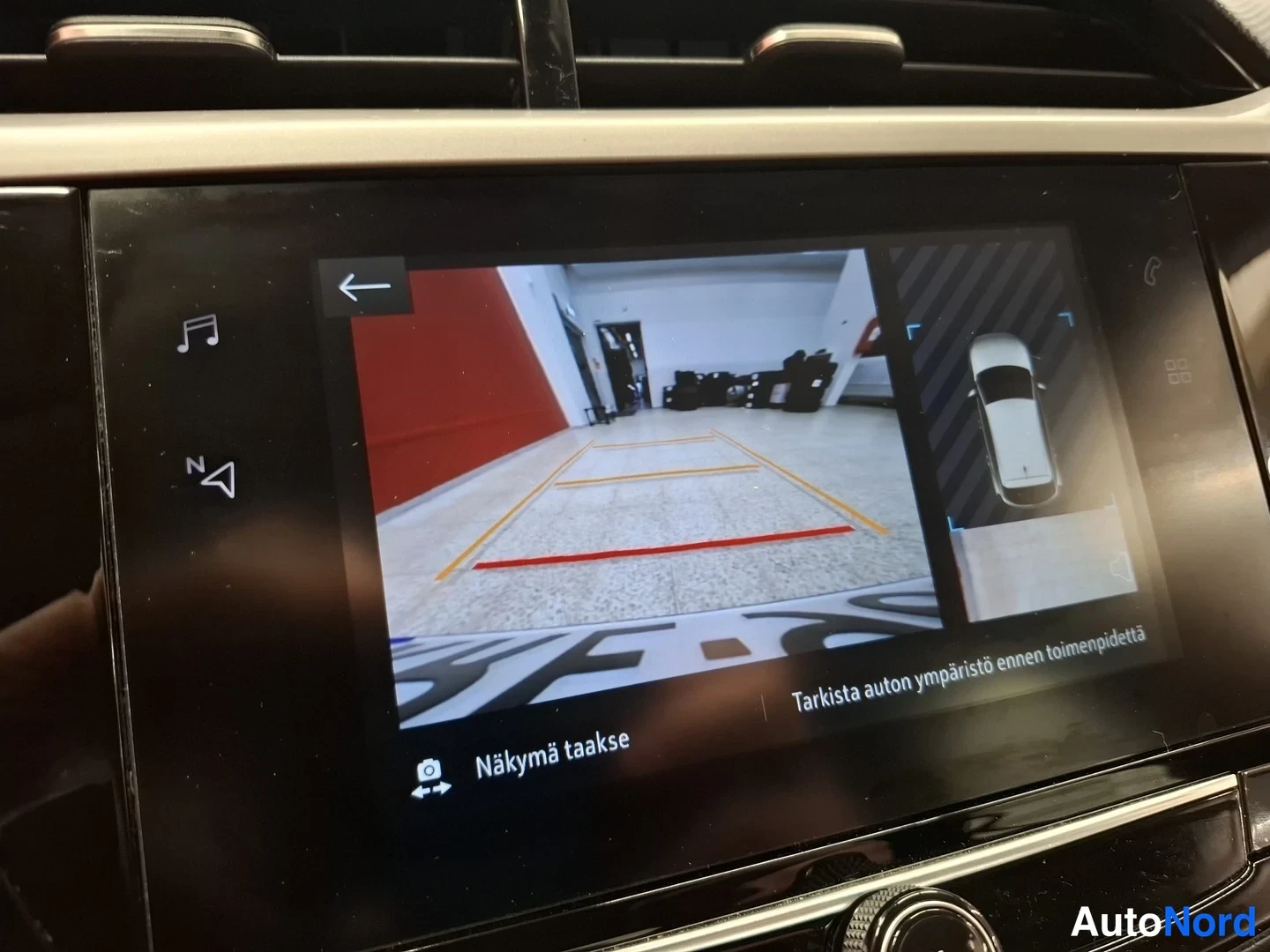 Muu: Kojelaudan infotainment-näyttö, jolla näkyy peruutuskameran kuva parkkihallista ohjausviivoineen sekä auton ympärivartalokuva.