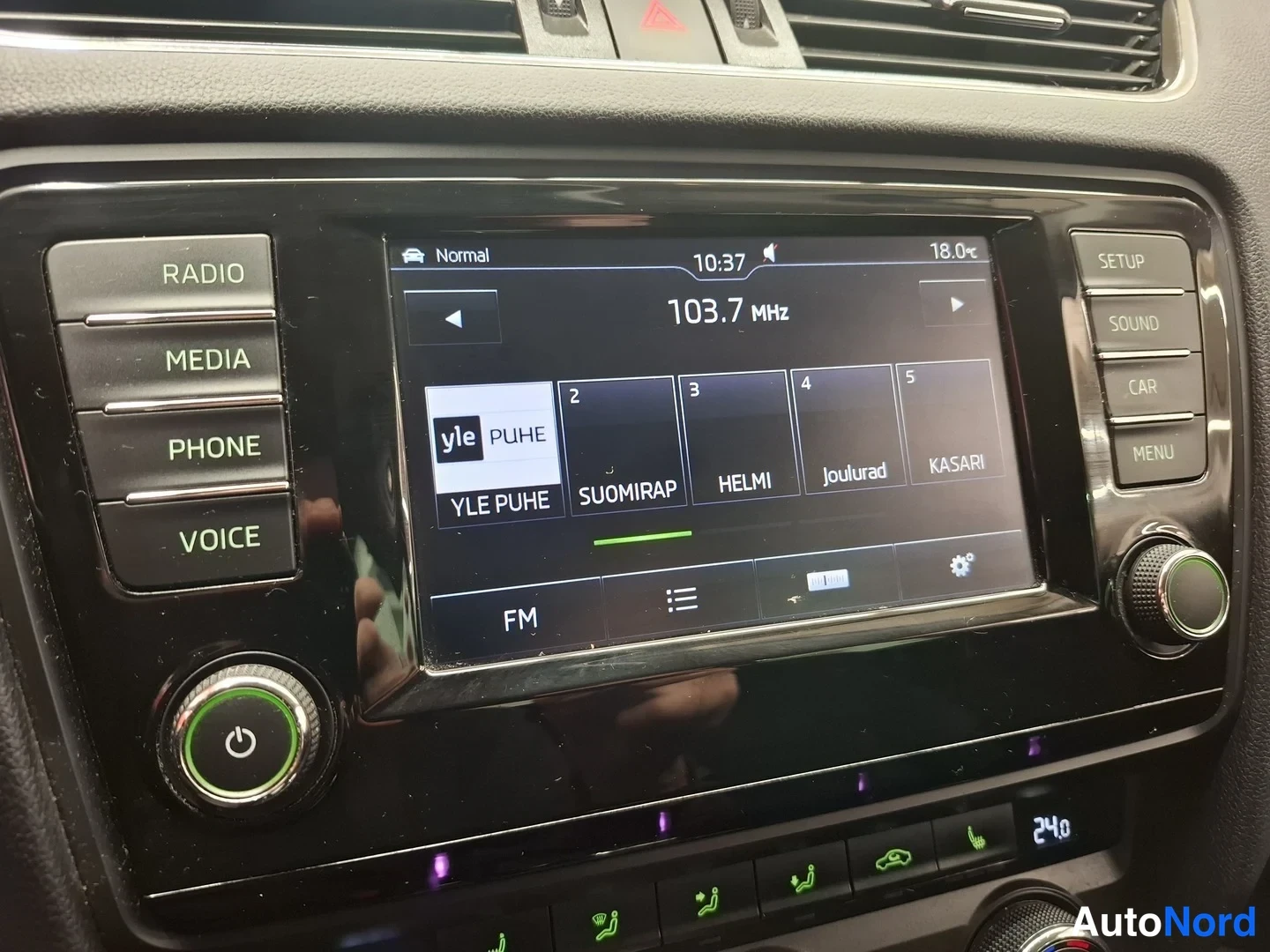 Muu: Kojelaudan radio: näytöllä FM 103,7 MHz ja kanavalista YLE PUHE, SUOMIRAP, HELMI, Joulurad, KASARI; sivussa RADIO-, MEDIA-, PHONE- ja VOICE-painikkeet.