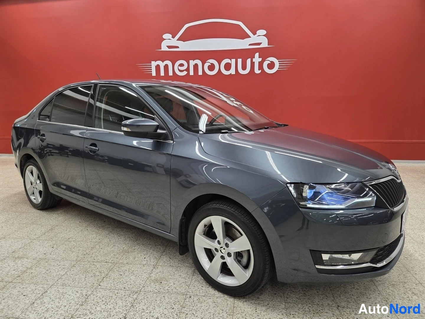 Etuviisto, nokka oikealle: Skoda Rapid -sedan etukulmasta oikealta, tummanharmaa kori ja hopeavanteet sisätiloissa.