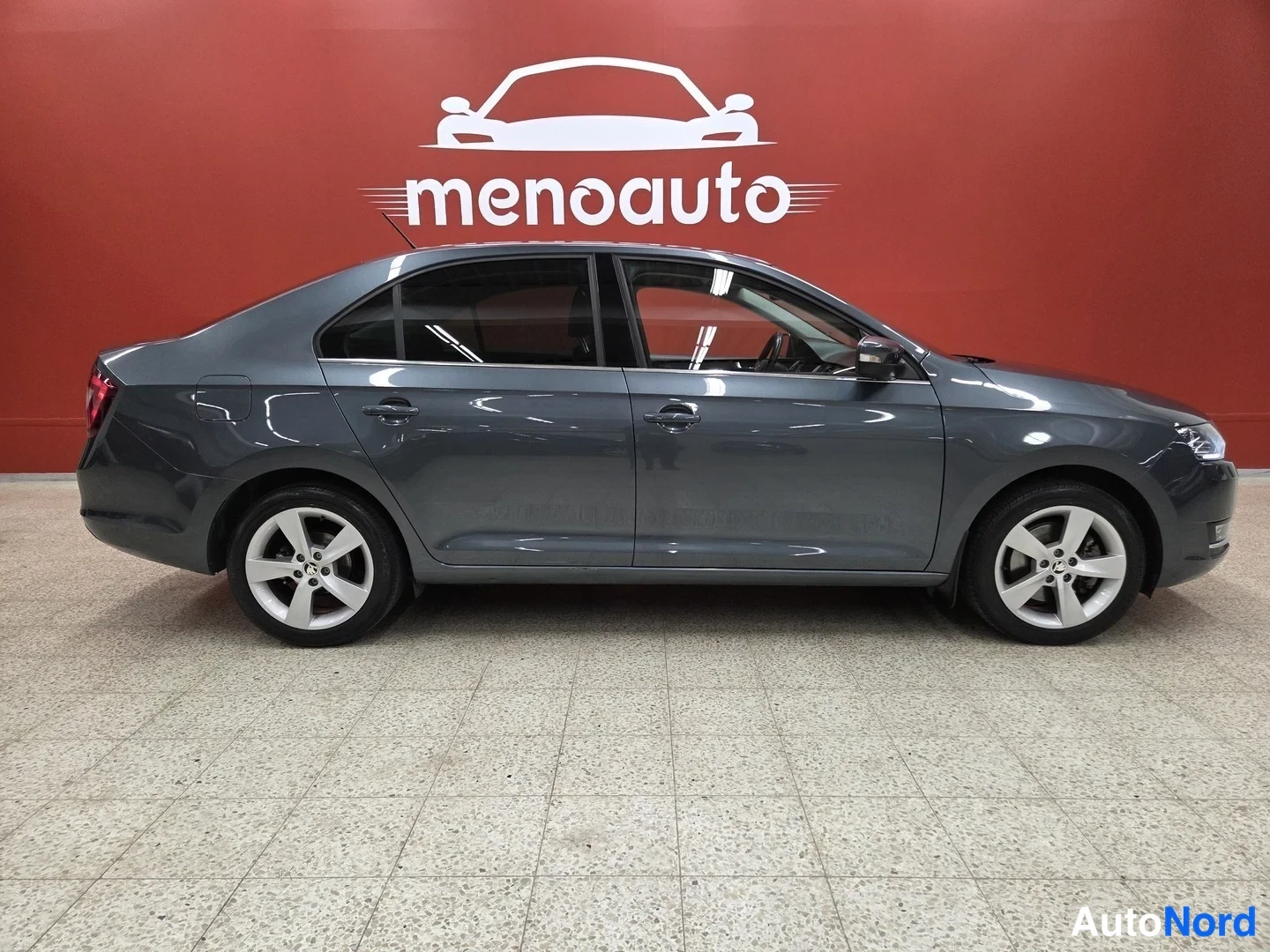 Sivulta: Skoda Rapid -sedan sivukuva vasemmalta, tummanharmaa kori ja hopeavanteet sisätiloissa.