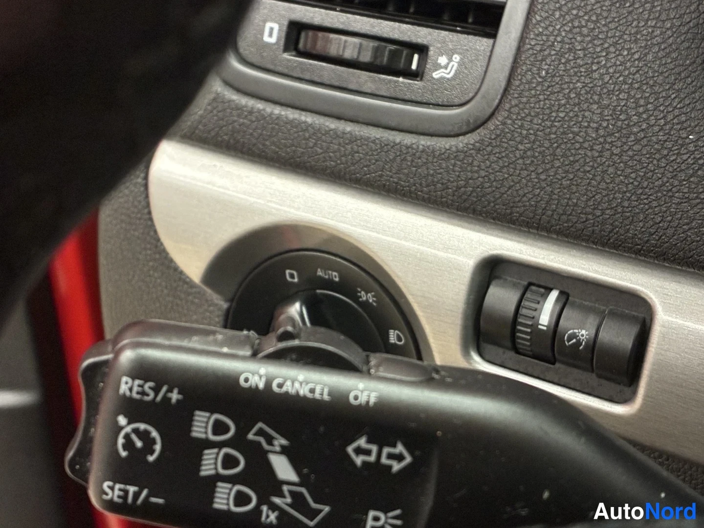 Yksityiskohta: Ohjaustason kytkimistö lähikuvassa: ajovalosarjan kytkin AUTO-merkinnällä, dashboardin säädin, lämmitetty istuin -symboli ja vakionopeudensäädön vipu RES/+ ja S