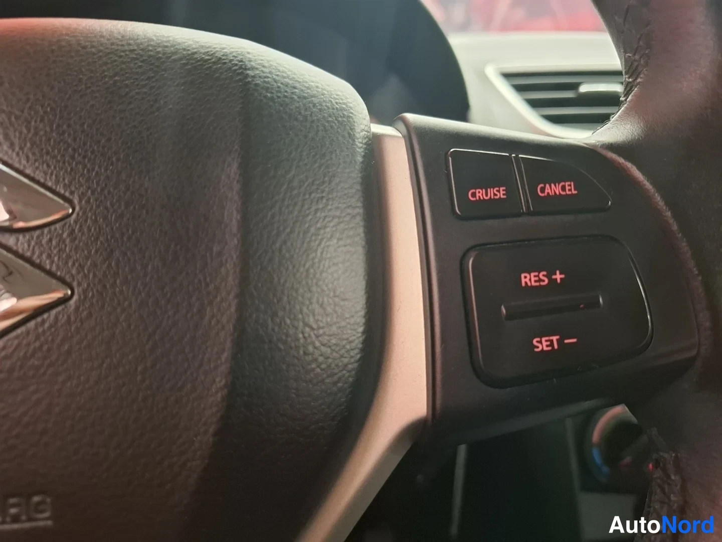 Yksityiskohta: Il lato destro del volante ha i tasti del tempomat CRUISE, CANCEL, RES + e SET −; sul volante è visibile il logo Suzuki.