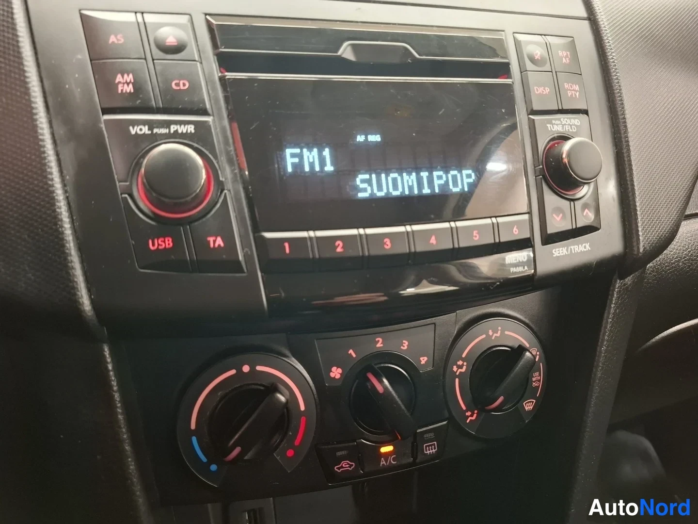 Yksityiskohta: La radio con lettore CD mostra 'FM1 SUOMIPOP'; sotto i cursori per volume e bilanciamento e tre cursori di climatizzazione con etichetta A/C.