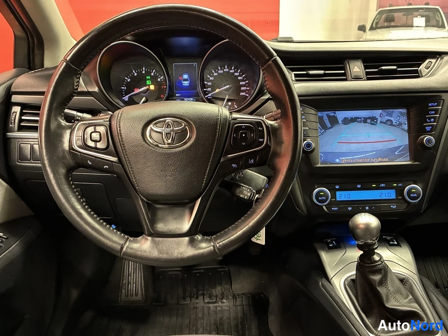 Muu: Toyota Avensisin ohjaamo: Toyota-merkkinen ohjauspyörä, kojetaulun mittarit, kosketusnäyttö ja manuaalivaihtoheitin.