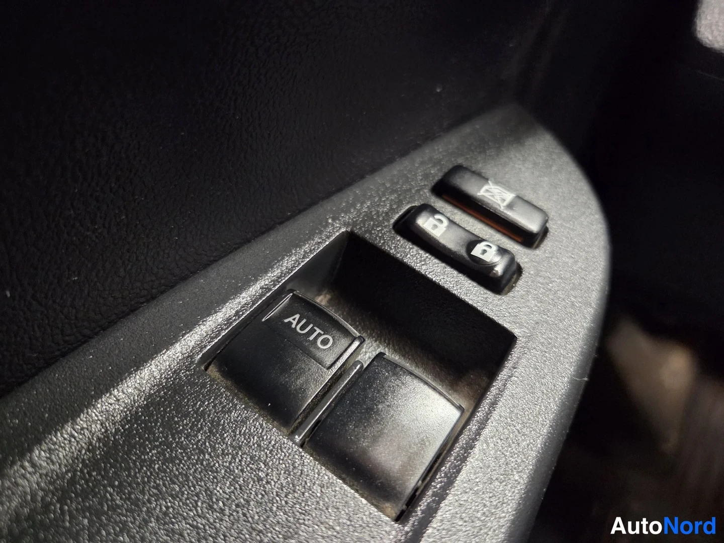 Muu: Lähikuva oven pystysäleikköstä: ikkunannostimen painike, jossa lukee 'AUTO', kaksiosainen lukituksen avaus- ja lukituspainike sekä ylhäällä lisäpainike.