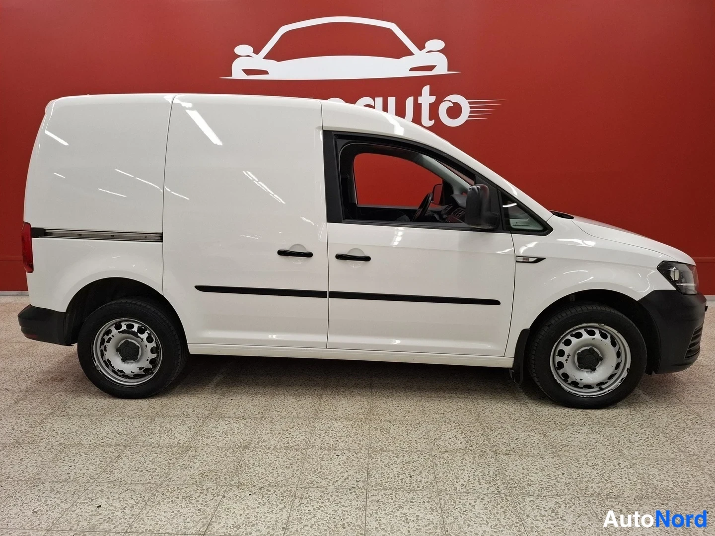 Etuviisto, nokka oikealle: Valkoinen pakettiauto sivulta oikealta, punainen taustaseinä.