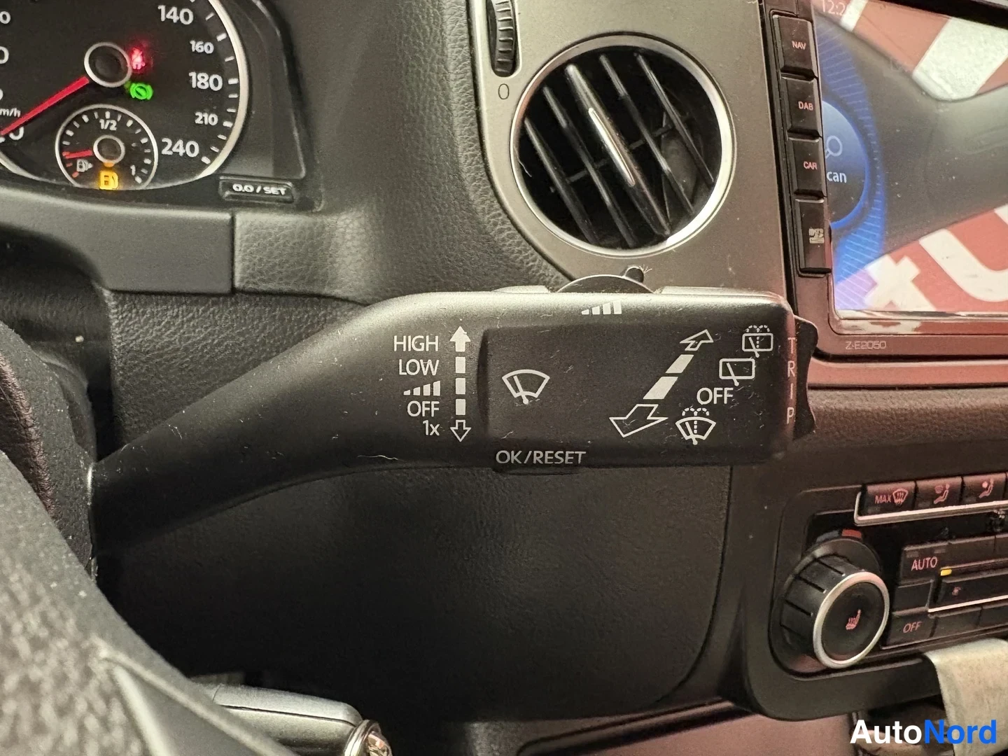 Yksityiskohta: Toimistoriste merkinnöillä HIGH, LOW, OFF, 1x ja OK/RESET, taustalla tähtimittaristo ja ilmastointipaneeli AUTO-napilla.