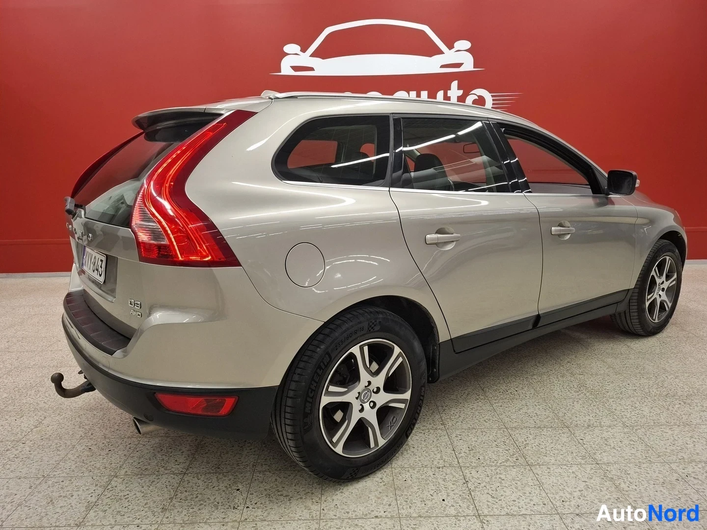 Takaviisto: Volvo XC60 -farmarin takakolmannelta kuvattu kuva, perä ja vasen kylki näkyvissä, messiinharmaa kori punaisella taustalla.