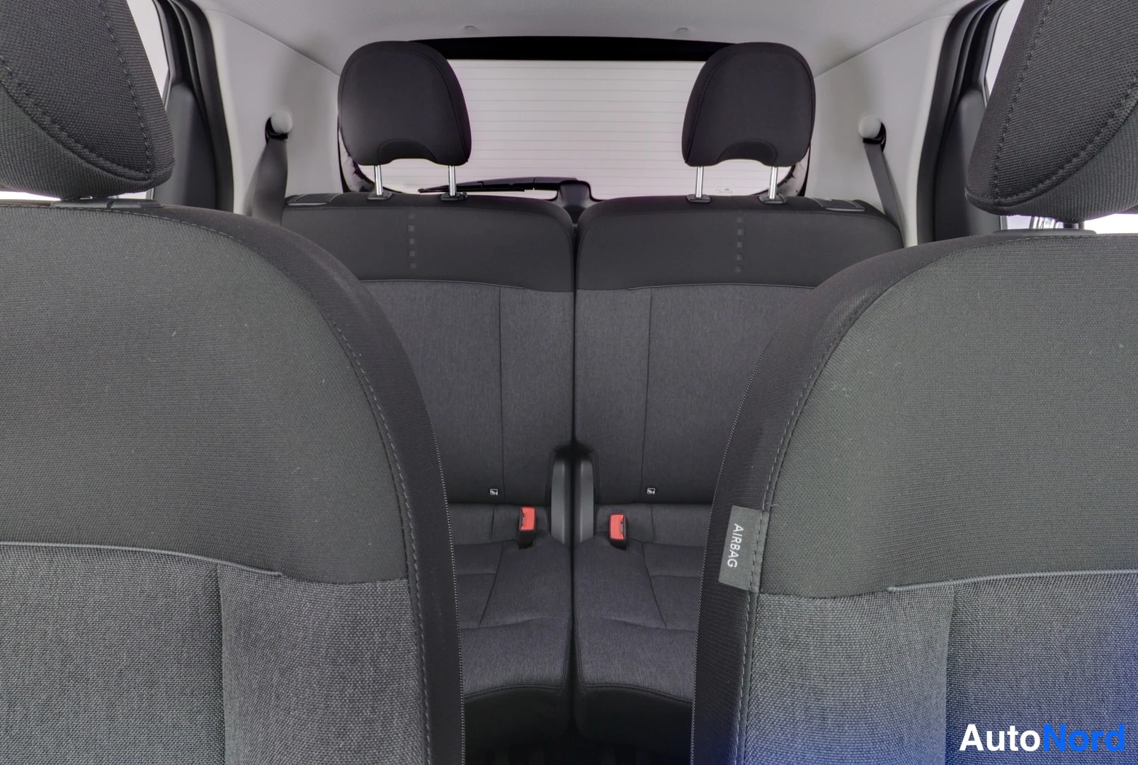 Muu: Takaistuimet kangasverhoiluinea takaa eteenpäin kuvattuna; etuistuinten AIRBAG-tarrat näkyvät.