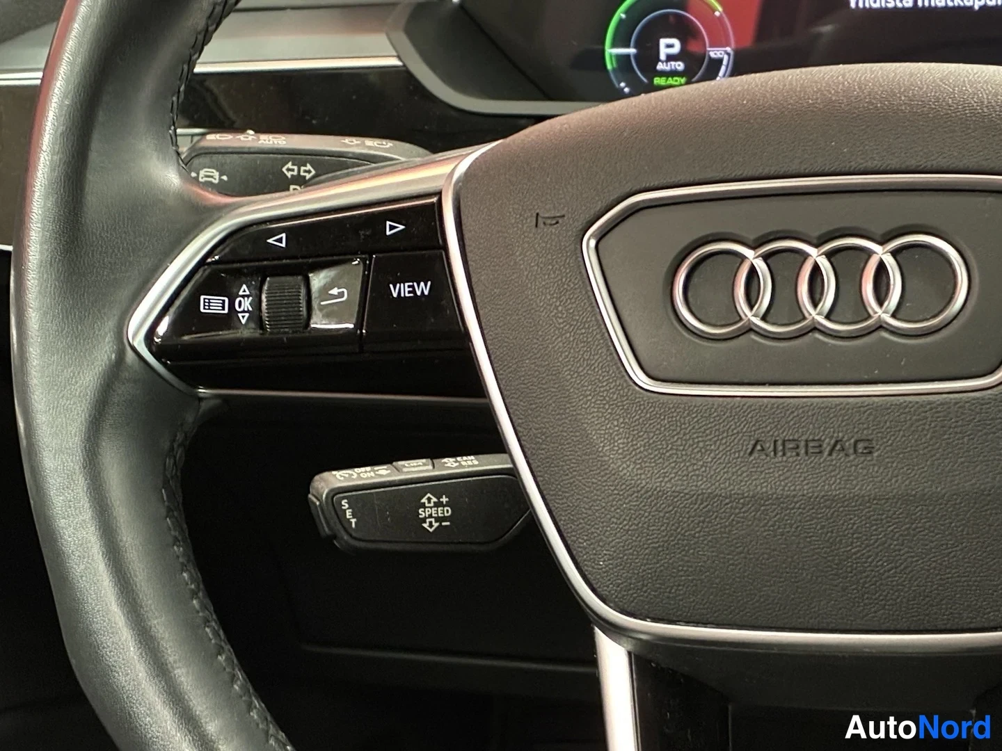 Sivulta: Audi-merkin ohjauspyörä, nappiryhmä VIEW ja OK sekä vivut puristuksella ja vikkelä NOPEUS VAIHTAA KÄTISYYTTÄ.
