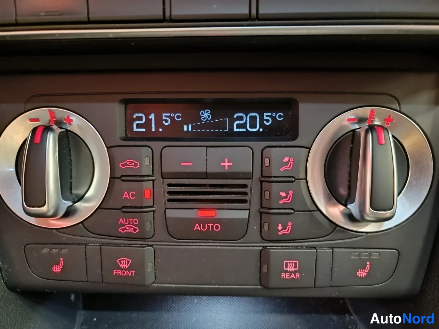 Muu: Audi Q3:n kaksivyöhykeinen automaattinen ilmastointipaneeli, näytöllä 21,5°C ja 20,5°C; paneelissa AC- ja AUTO-napit sekä istuinten lämmitys ja etu- ja takalasi