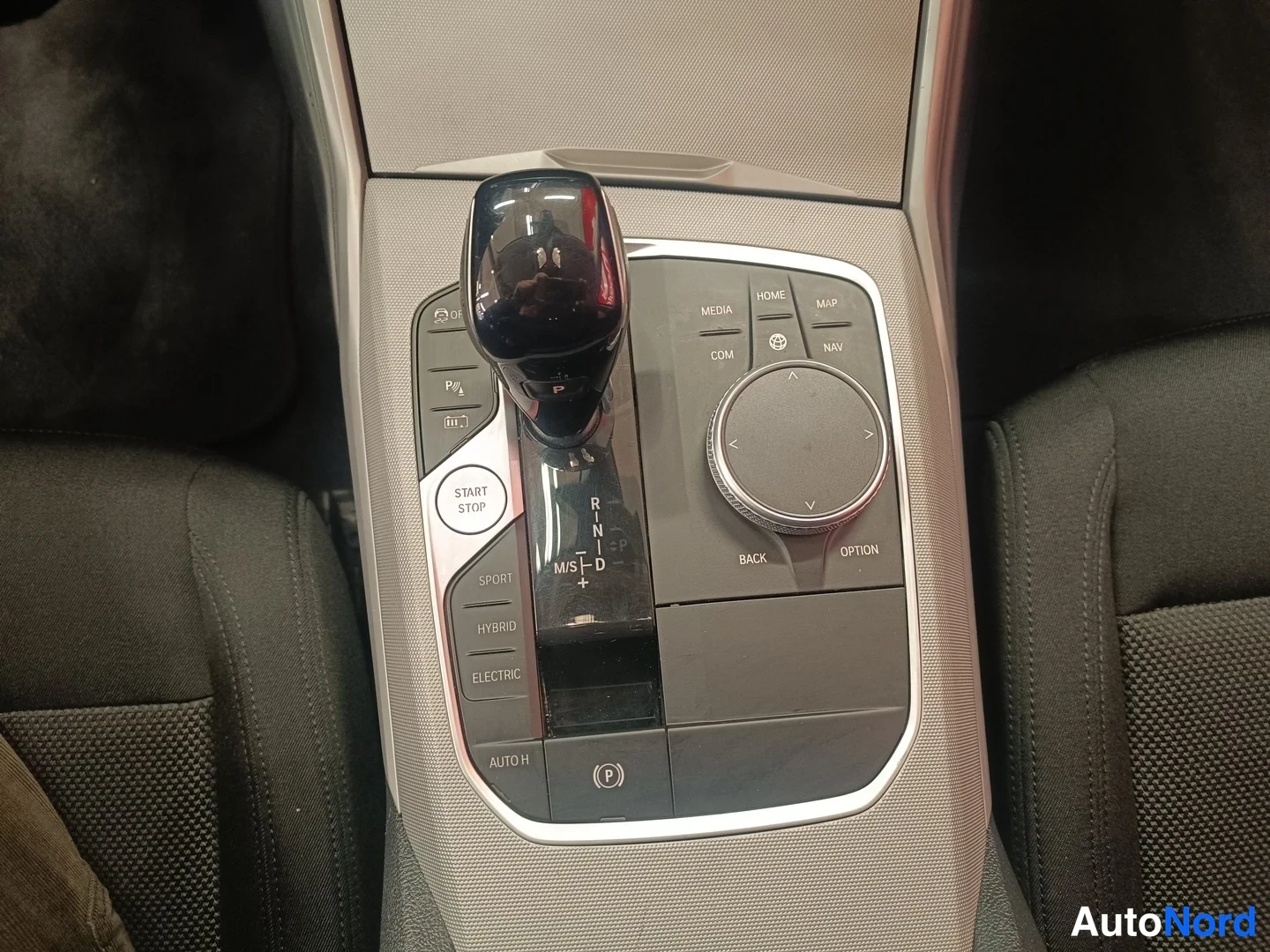 Muu: Auton keskikäytävä: automaattivaihteen valitsin ja iDrive-ohjain, jossa näkyvät painikkeet Start Stop, Sport, Hybrid ja Electric.