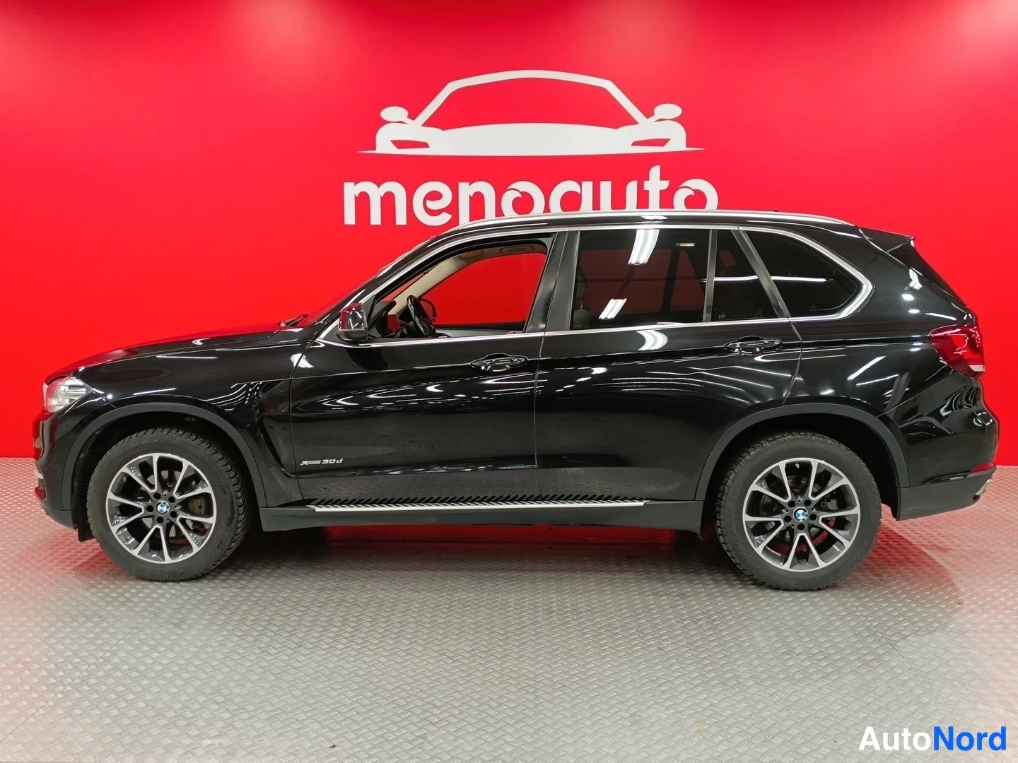 Sivulta: BMW X5:n sivukuva oikealta puolelta, musta SUV punaisella taustalla.