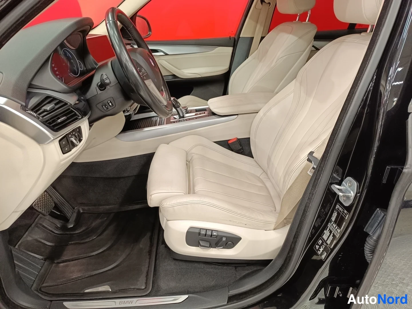 Muu: BMW X5:n sisätilat kuljettajan puolelta: beige nahkapenkit, ohjauspyörä ja istuinsäätimet.