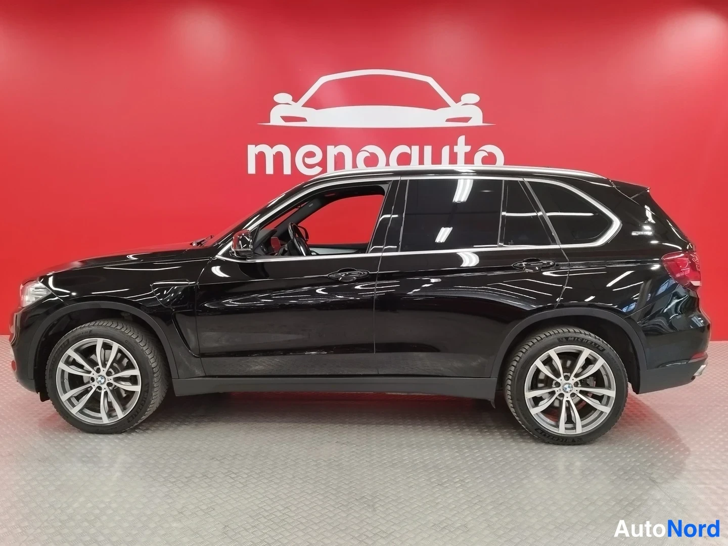 Sivulta: Mustan BMW X5 -maasturin sivukuva oikealta puolelta punaisen taustan edessä.