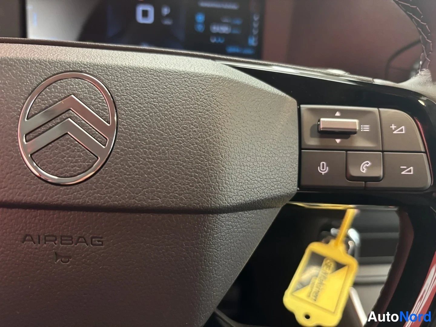 Muu: Ohjauspyörän oikea puoli lähikuvassa: Citroën-logo, AIRBAG-teksti ja nappiryhmä puhelin- ja äänikommilla; keltainen avainnipun roikkumassa.