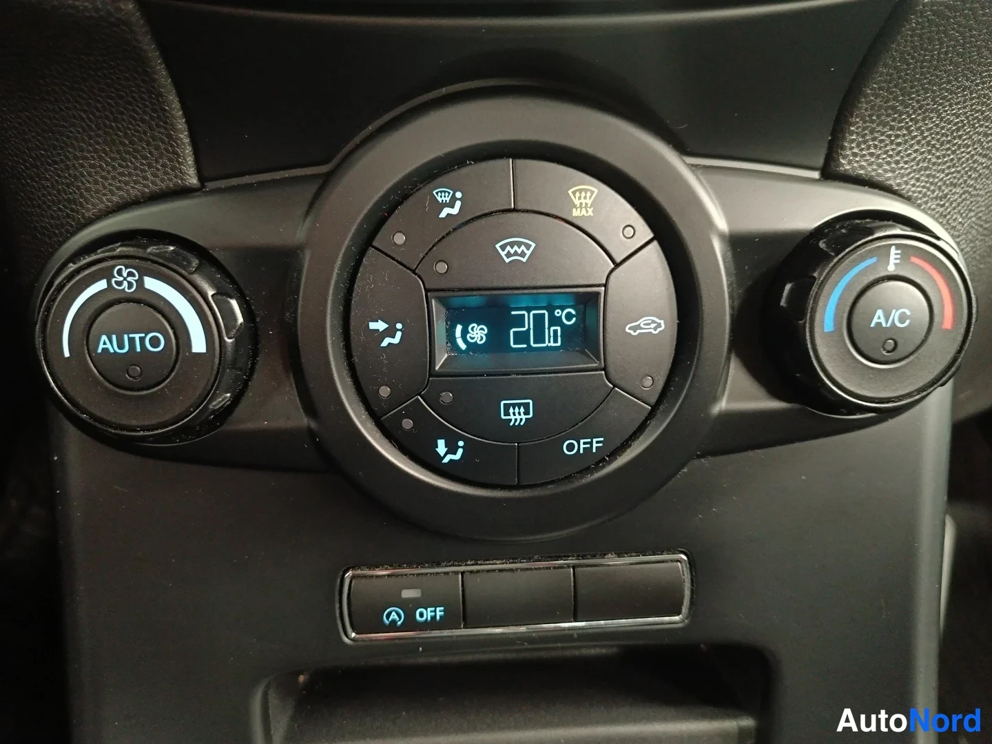Yksityiskohta: Tarkennettu kuva ilmastointipaneelista: pyöreä automaattisen ilmastoinnin säädin, näyttö 20 °C, A/C-merkitty nappi, OFF- ja start/stop-painikkeet.
