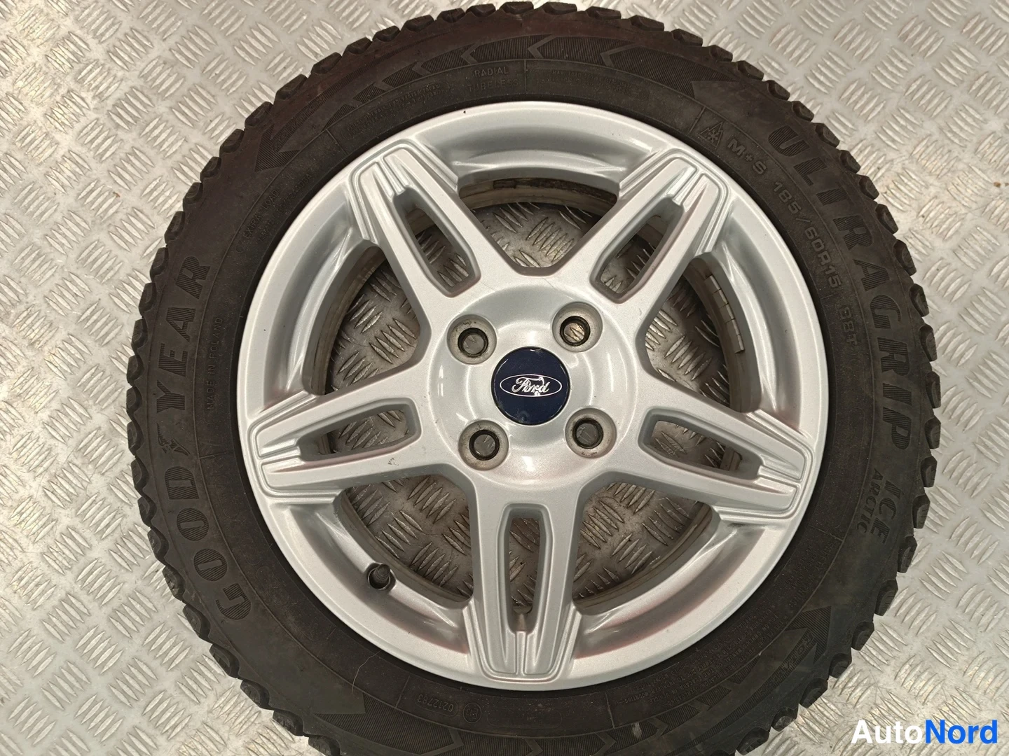 Yksityiskohta: Hopeanvärinen viisikeskarkonen ahtaus Toyota-logolla ja Goodyear UltraGrip-tes renkaassa, varattuna 195/60 R16 M+S, esteettisesti hyväkuntoisena.