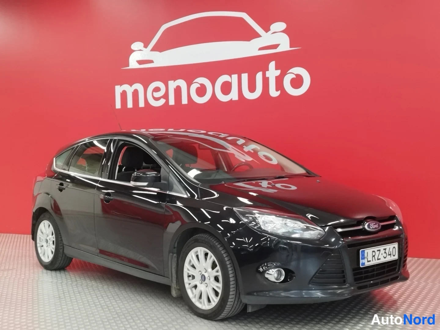 Etuviisto, nokka oikealle: Mustan Ford Focus -henkilöauton etukulma punaisella taustalla, etupanssari ja konepelti näkyvät.