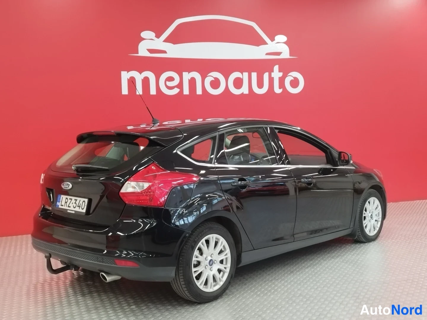 Takaviisto: Mustan Ford Focus -henkilöauton takakulma punaisella taustalla, takavalot ja rekisterikilpi näkyvät.