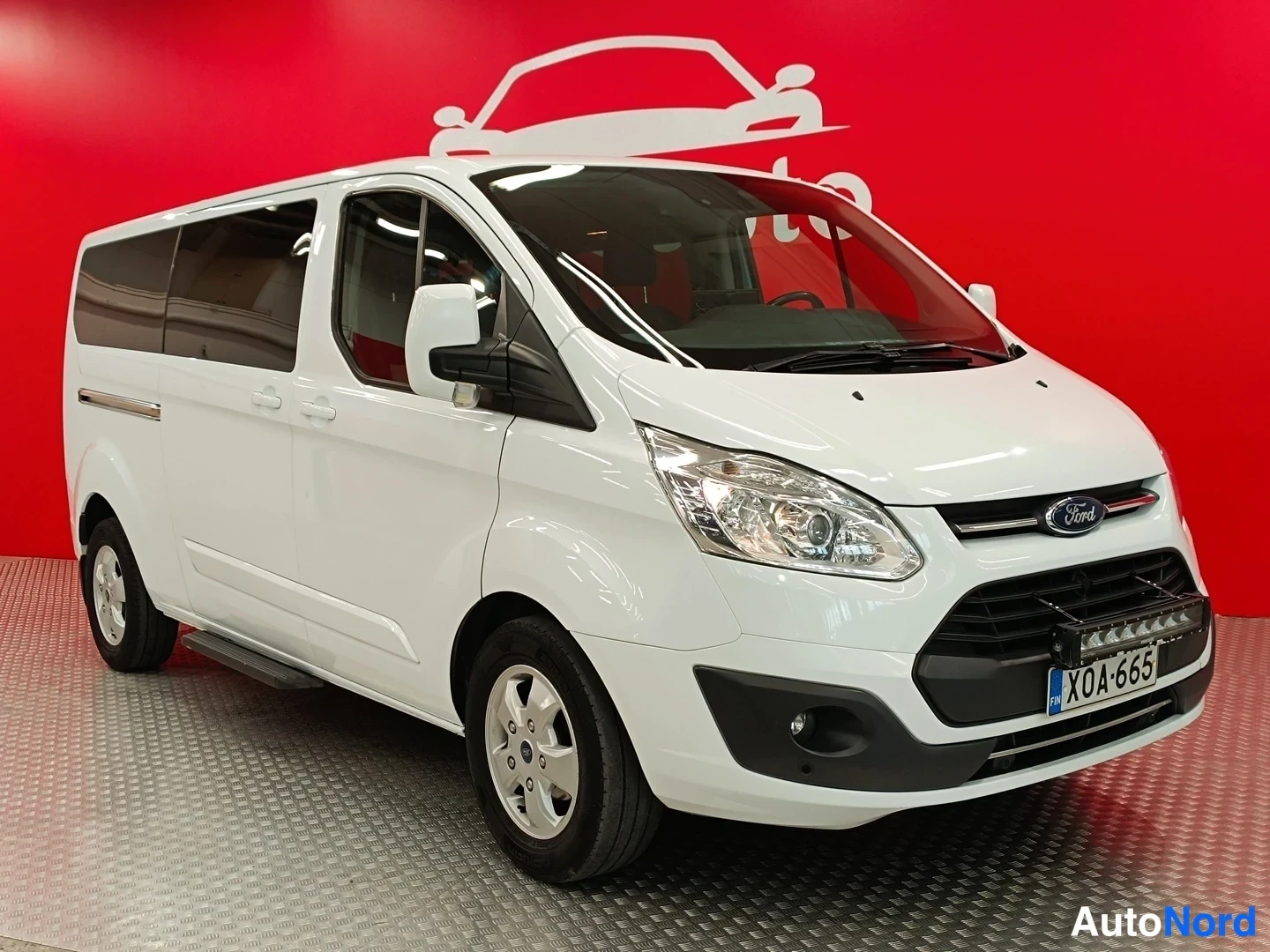 Etuviisto, nokka oikealle: Ford Tourneo Custom -pakettiauto edestä vasemmalta kuvattuna, valkoinen koripaneli ja kylki näkyvät.