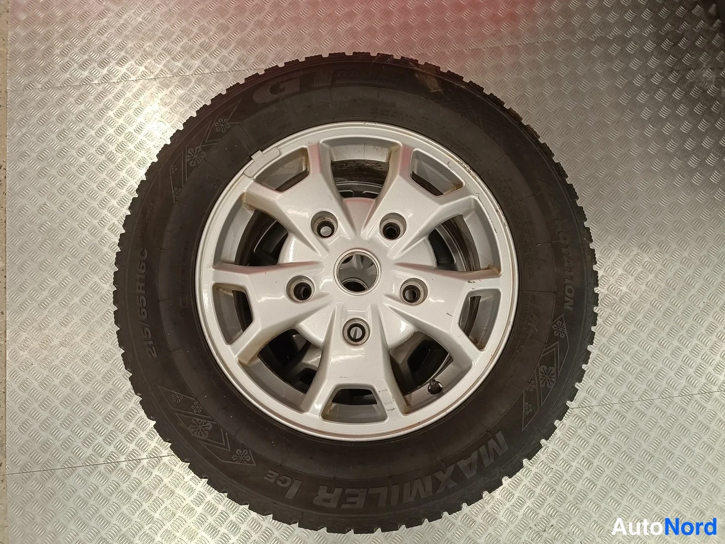 Yksityiskohta: Talvirengas hopeanvärisellä vanteella alumiinilevyllä; rengasmerkintä Maxmiler Ice 215/65R16C.