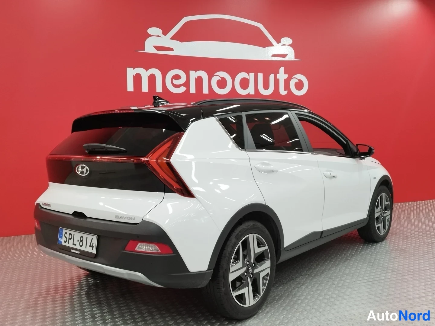 Takaviisto: Valkoinen Hyundai Bayon takaviistosta, musta luukku ja LED-takavalot, rekisteri, punainen taustaseinä.