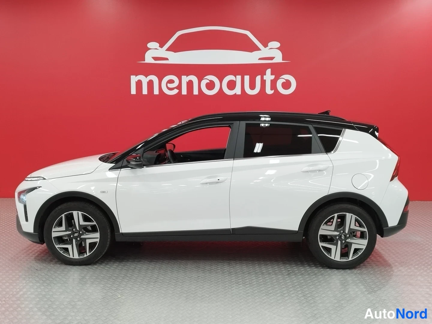 Sivulta: Hyundai Bayon -maasturin sivuprofiili: valkoinen kori ja musta katto, auton vasen sivu kuvassa punaisella taustalla.