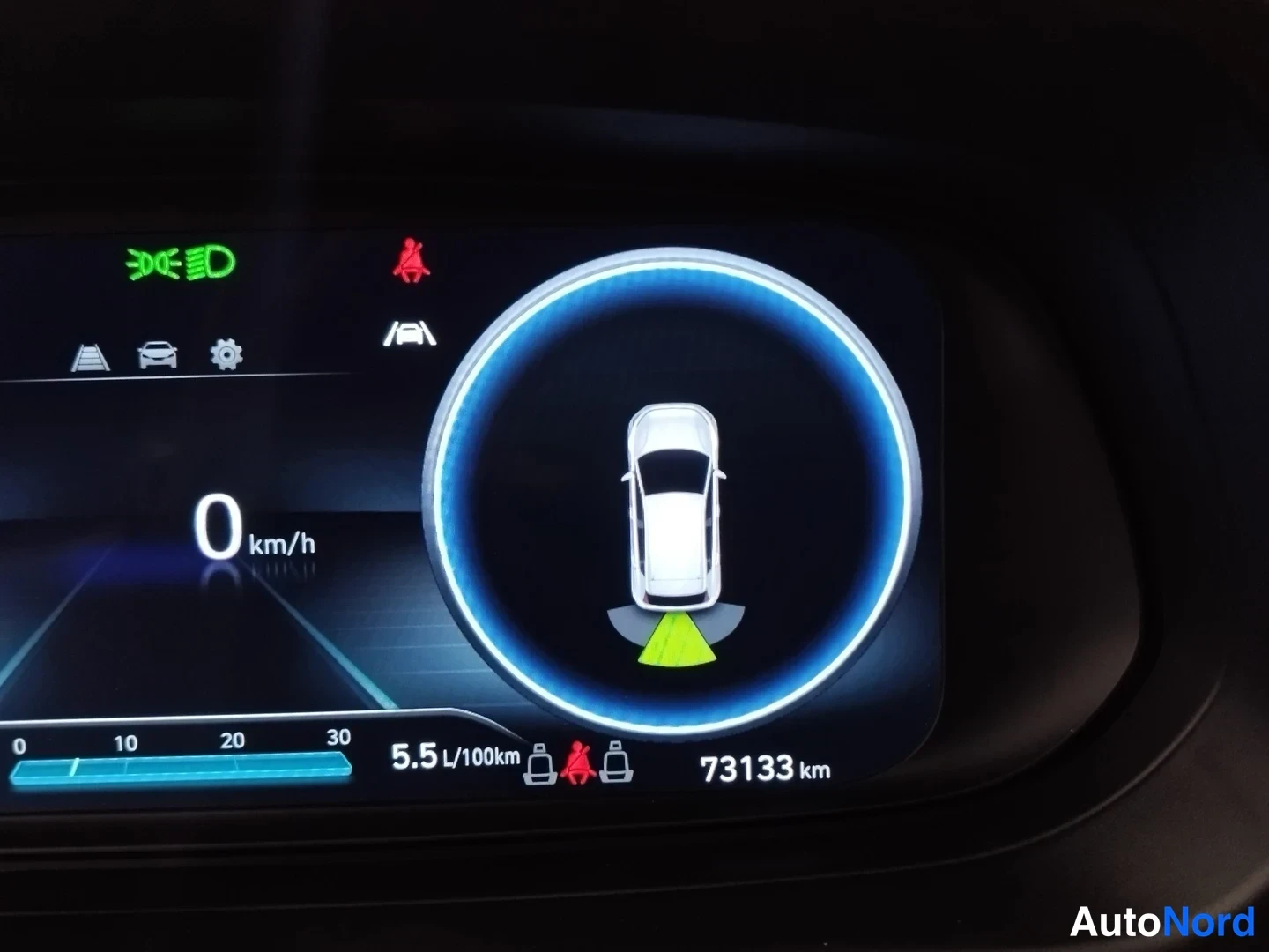 Edestä: Digitaalinen mittaristo suurennuksessa: nopeus 0 km/h, ajokilometrit 73133 km, keskellä auton kuva ympyrässä ja polttoaineenkulutus 5,5 l/100km.