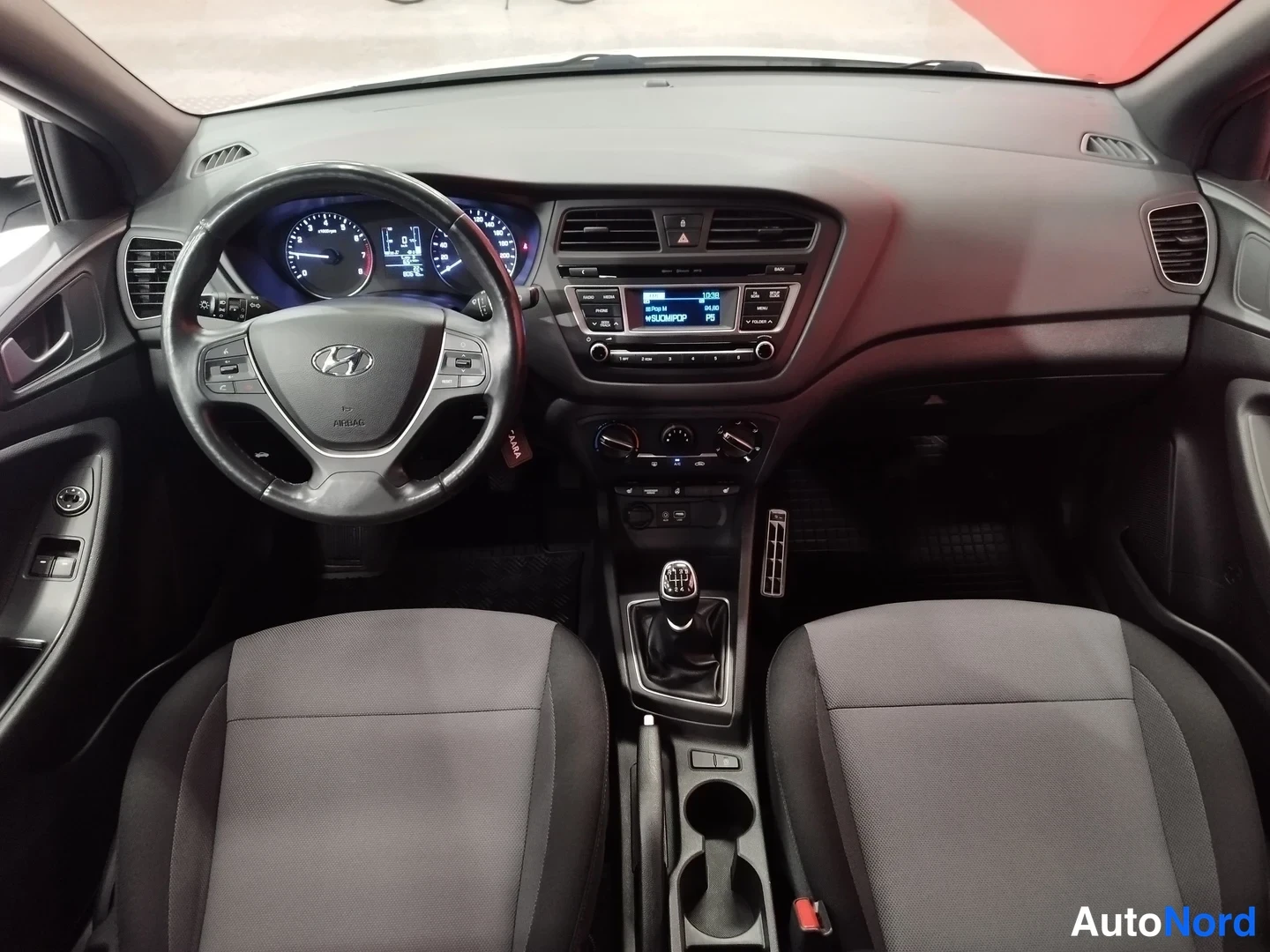 Muu: Hyundai i20:n ohjaamo edestä: manuaalivaihteisto, radio ja mittaristo.
