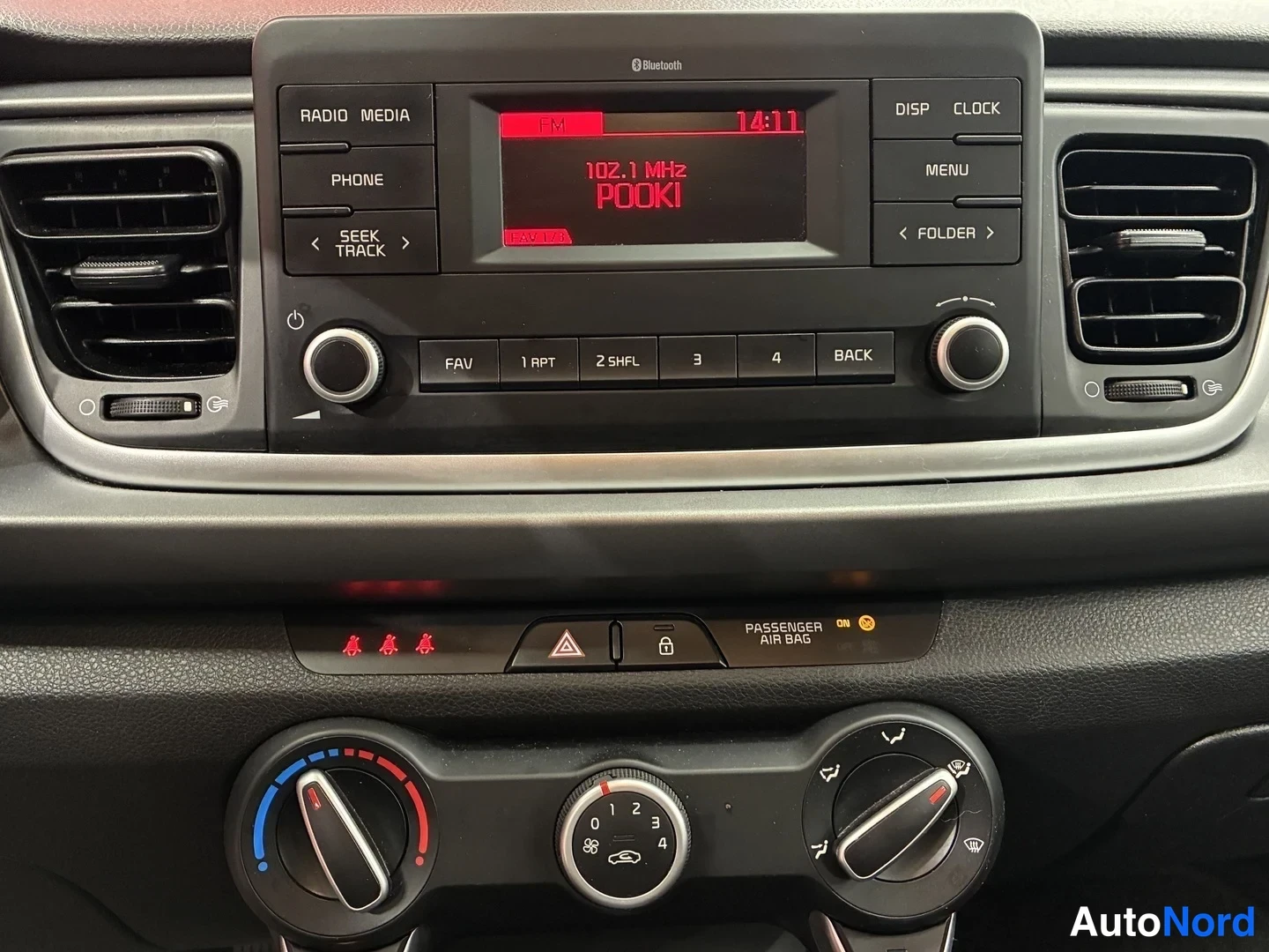 Edestä: Kojelauta: radio joka näyttää 102.1 MHz ja kellonaika 14:11, manuaaliset ilmastointisäätimet.
