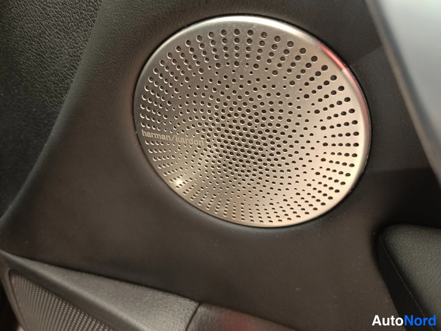 Muu: Auton ovipanelissa pyöreä harman/kardon-merkitty kaiutin metallireunalla, mustassa panelissa.
