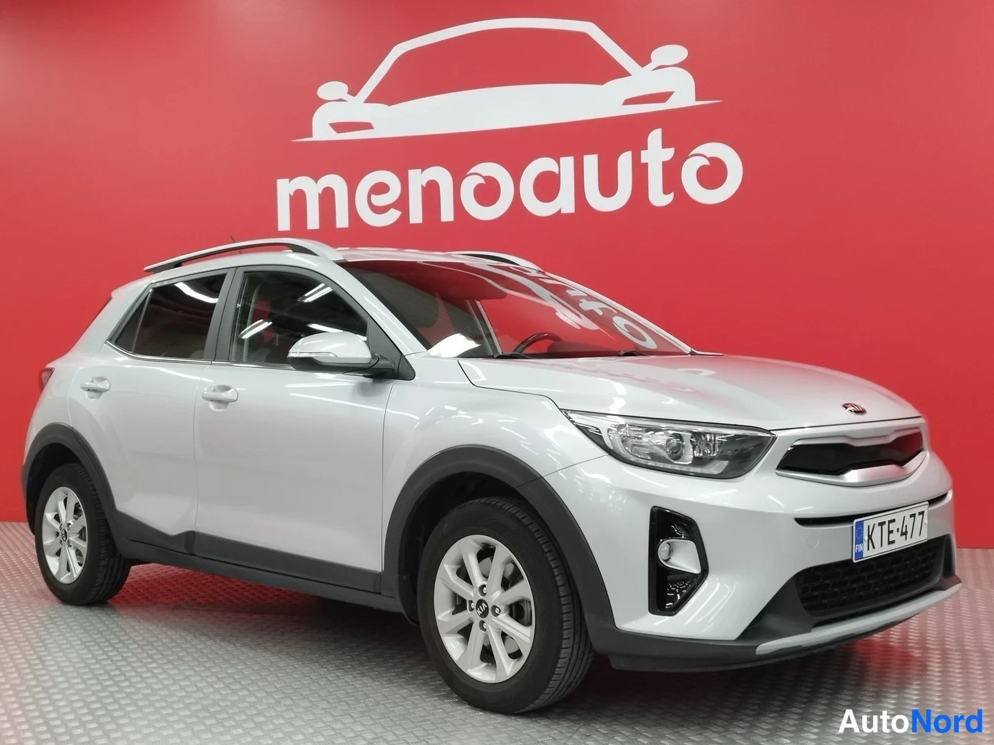 Etuviisto, nokka oikealle: Kia Stonic -henkilöauto etukulmasta oikealta, hopeanvärinen, rekisteritunnus, menoauto-tausta.