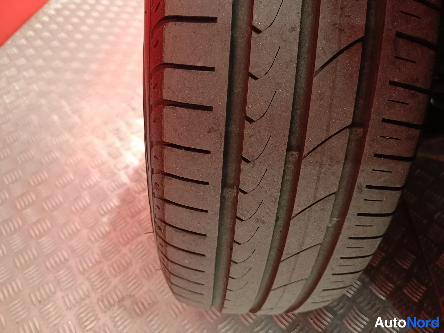 Yksityiskohta: Lähikuva renkaan urapinnasta vaalealla ruudullisella pohjalla; kulutuspinta näkyy tarkasti.