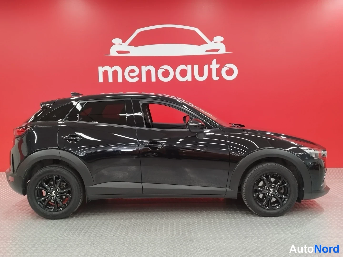 Sivulta: Mustan Mazda CX-3:n sivukuva vasemmalta, rekisteri ei näy, punainen menoauto-tausta.