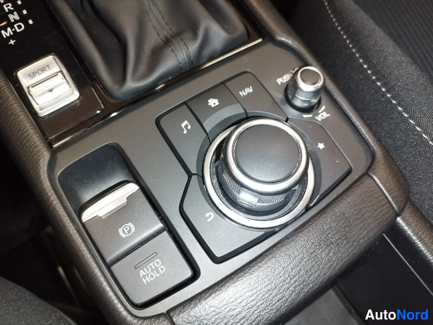 Muu: Vaihtajan vieressä oleva keskihalli: elektronisen seisontijarrun (P) painike, AUTO HOLD -painike, SPORT-kytkin ja Mazda-infoentertainmentin kierto-ohjain.