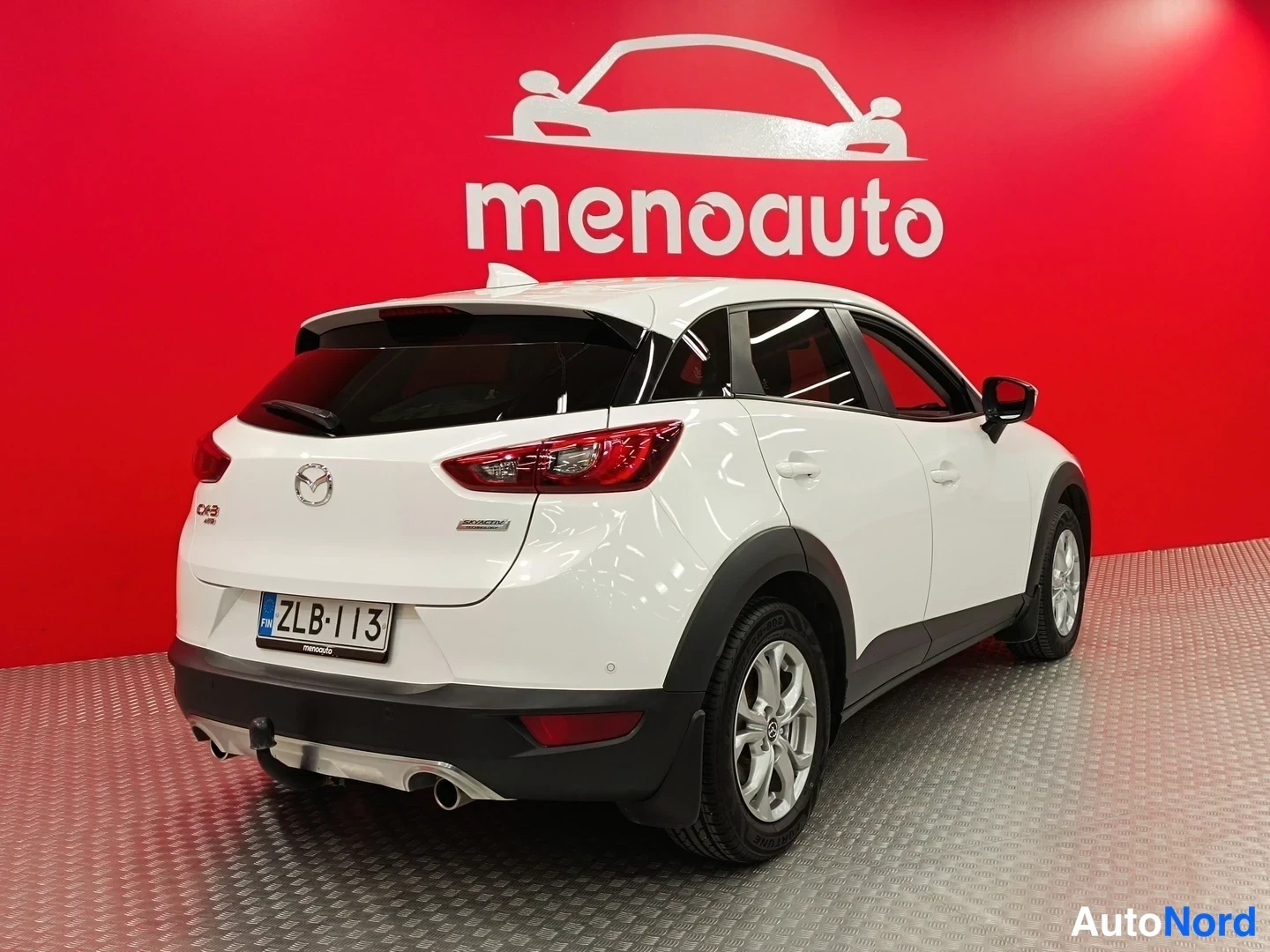 Takaviisto: Valkoinen Mazda CX-3 -henkilöauto takakulmasta, rekisterikilpi, punainen menoauto-tausta.